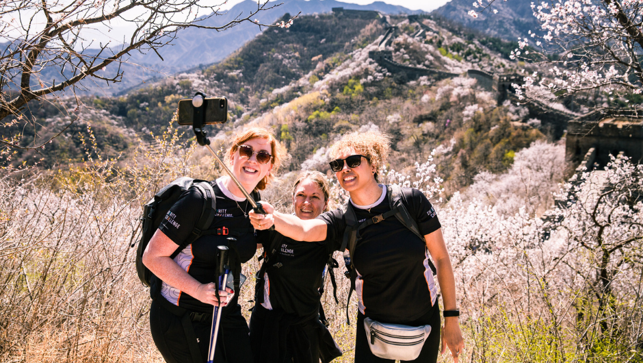 A group of people wearing Charity Challenge t-shirts and taking a photo with a selfie stick, whilst on a section of the Great Wall in China.