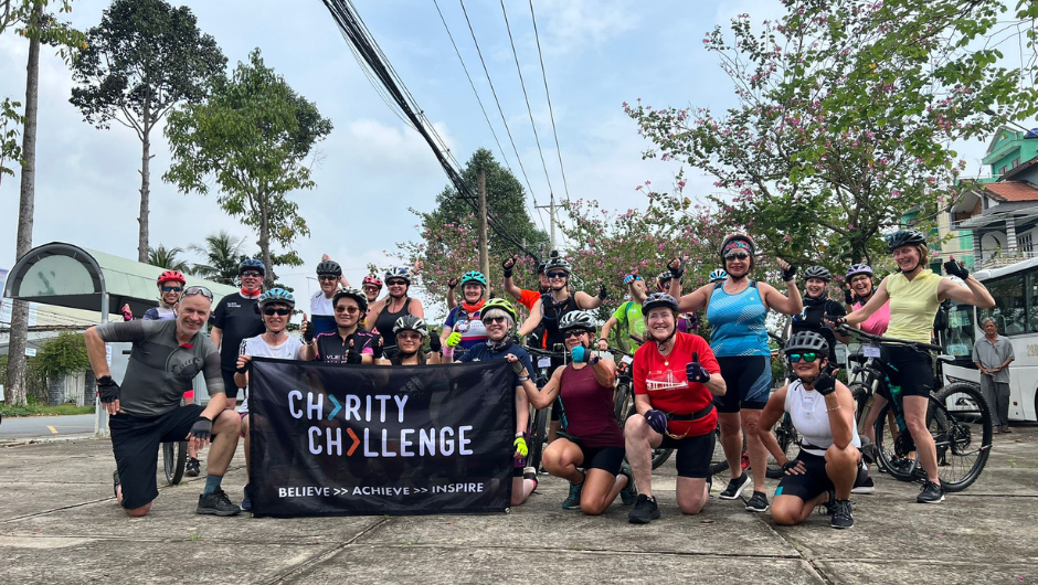 a group of cyclists wearing cycle gear, holding up a Charity Challenge flag during their Saigon to Angkor Wat Bike Ride challenge