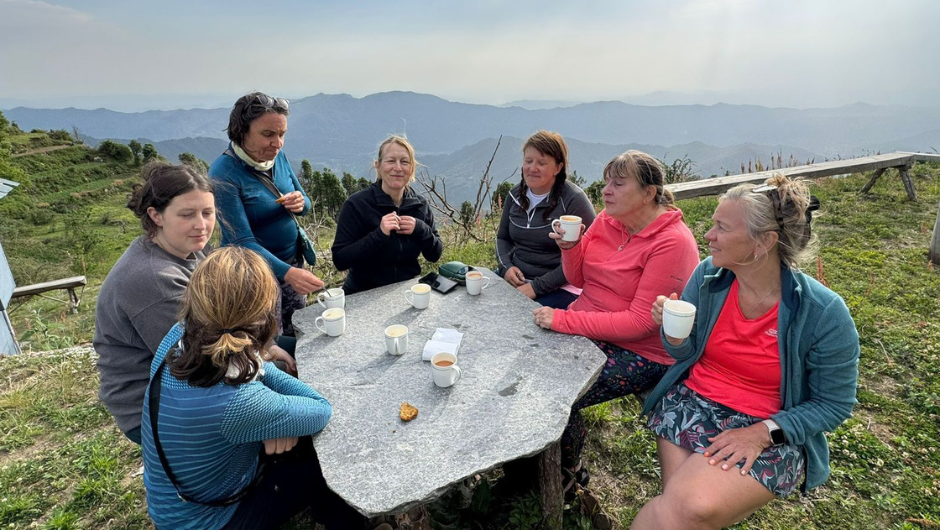 A group of people sitting around a table, drinking tea and talking at their campsite in the indian himalayas.