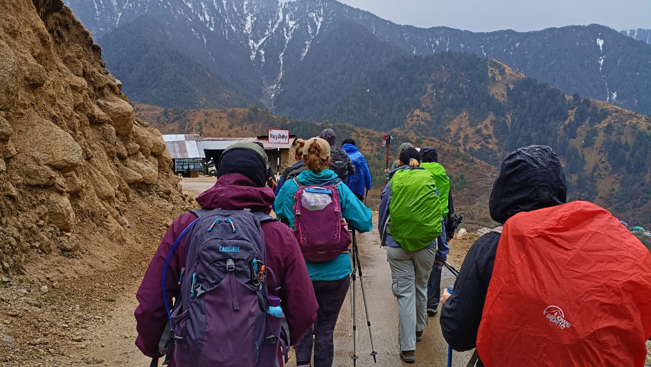 A group of trekkers, wearing rain jackets walking along a path, surrounded by mountains.
