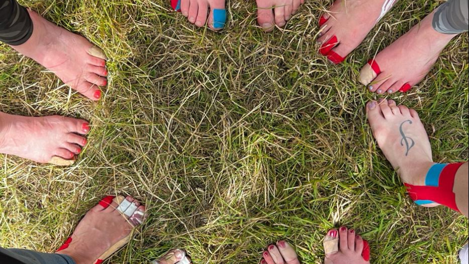 a circle of bare feet stood in the grass, each taped up with plasters or kinesiology tape.