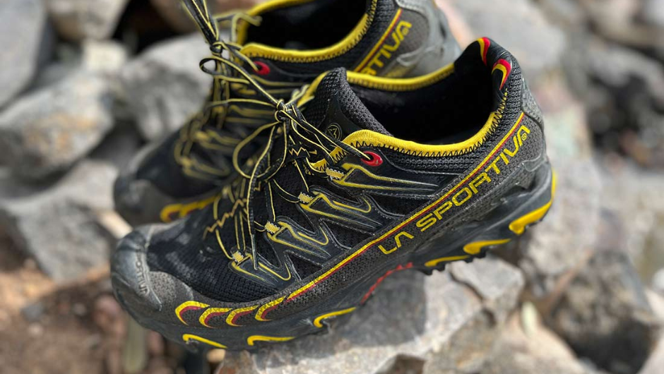 a pair of black and yellow trail shoes balanced on a rock