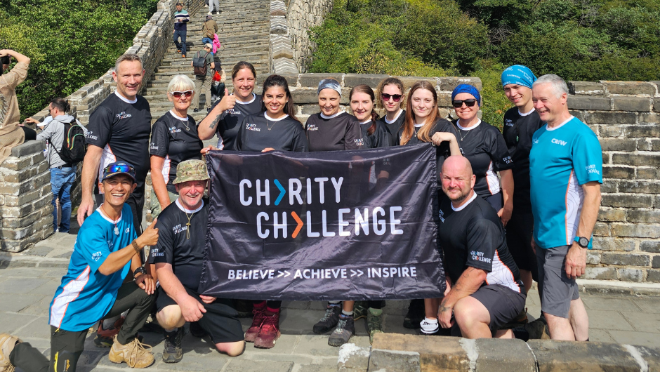 A group of trekkers and their local guide holding up a charity challenge sign on their great wall discovery challenge.
