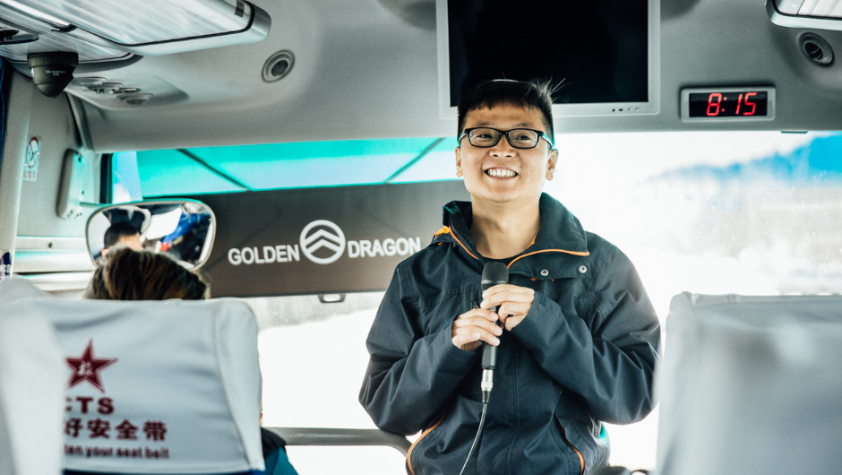 a local chinese guide standing with a microphone at the front of a tour bus.