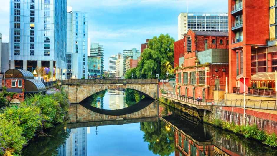 a section of manchester's canals, reflecting the buildings surrounding it and the bridge across it.