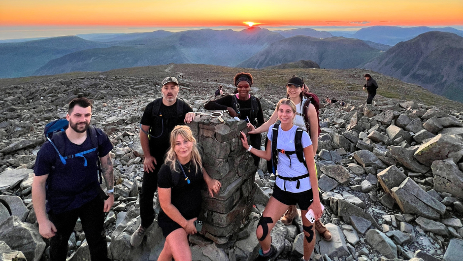 a group of trekkers at the summit of a mountain at sunrise, during their national three peaks challenge