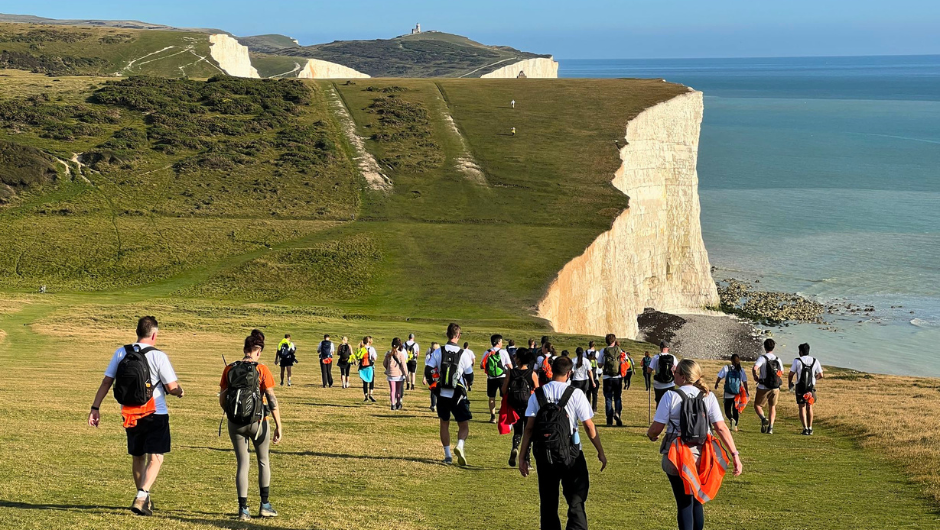 a large group of trekkers walking along the seven sisters cliffs, in the south downs national park