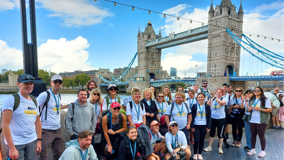 a group of challengers wearing their medals and posing for a celebration photo in front of tower bridge in london, after completing their thames footpath challenge