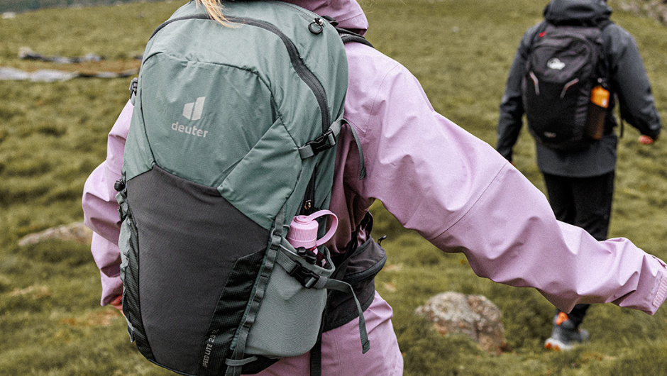 A person trekking, wearing a rain coat and a daypack.