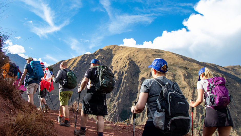 A group of people trekking up a steep slope, using walking poles and wearing daypacks.
