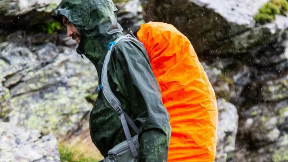 A person walking in the rain with a daypack covered by it's rain cover.
