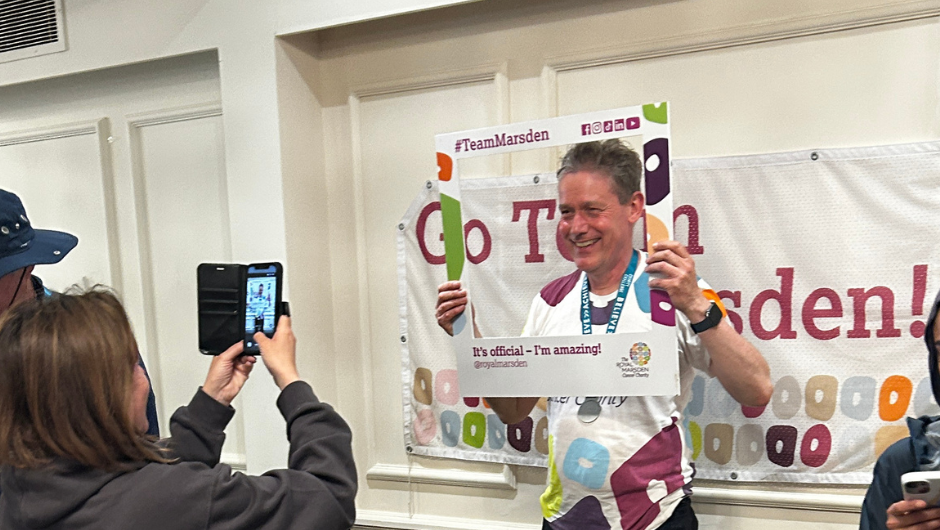 A trekker posing for a photo with a branded frame, after completing their charity challenge for the royal marsden cancer charity.