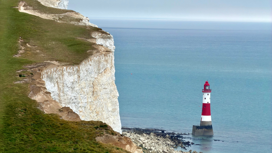 A section of the white Seven Sisters Cliffs in the South Downs next to the blue sea, and a red and white lighthouse.