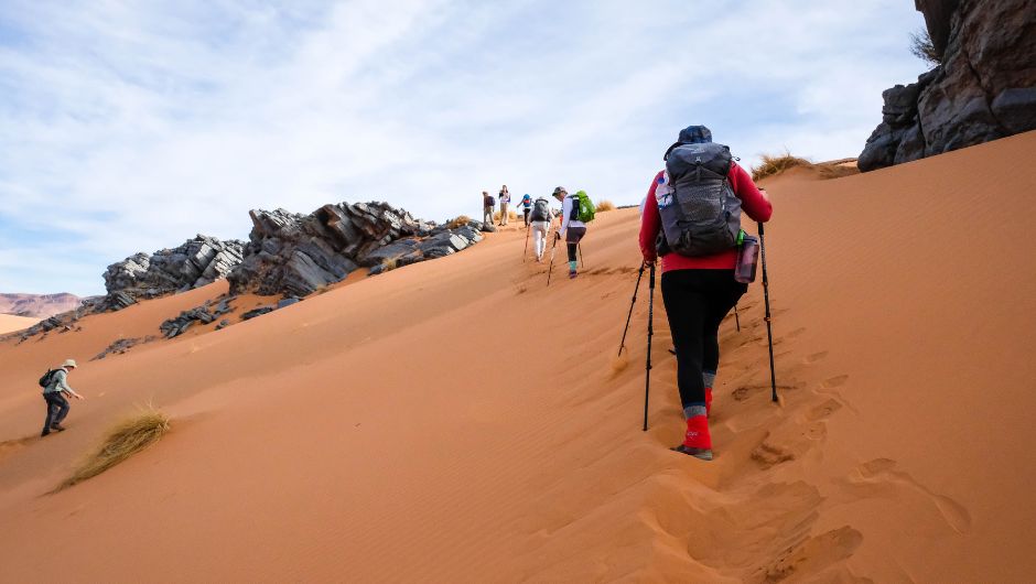 people trekking up a steep sand dune in the sahara