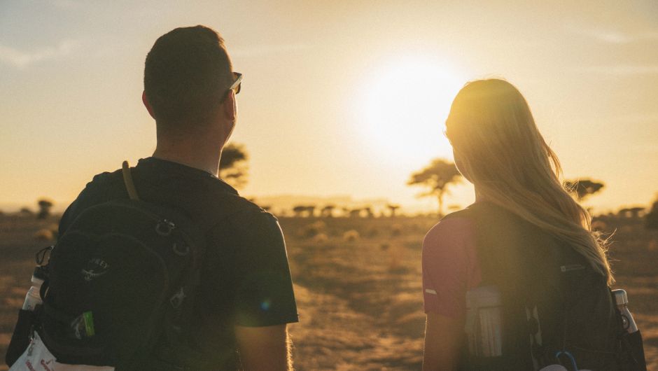 Two people looking towards a glowing sunset in the sahara desert, morocco