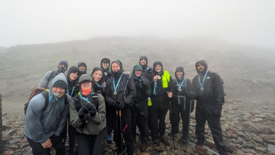trekkers dressed in rain coats and wearing charity challenge medals at the summit of a rainy mountain