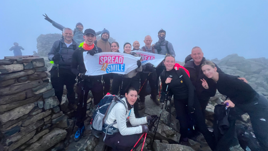 a group of trekkers smiling at the summit of a mountain during their national three peaks challenge