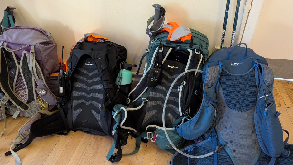 four backpacks packed and prepped with kit, trekking poles and water bottles