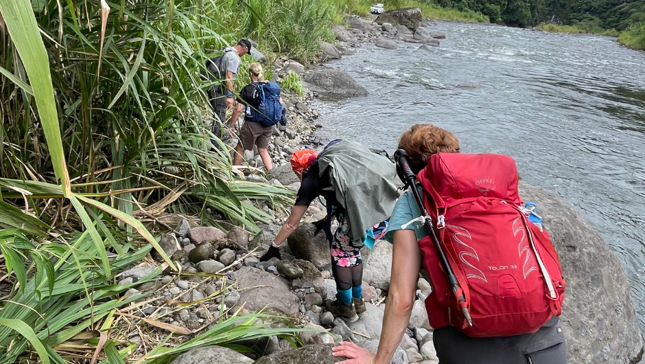 trekkers walking alongside a riverbed, wearing daypacks