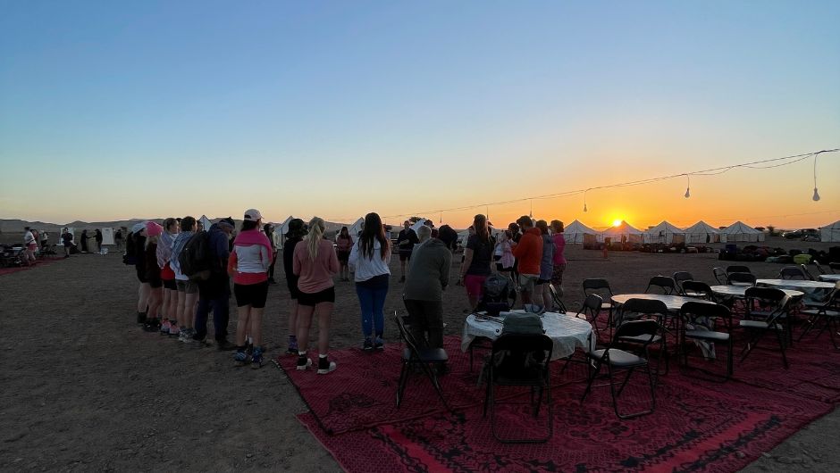 A group of people talking together at a campsite during sunset.
