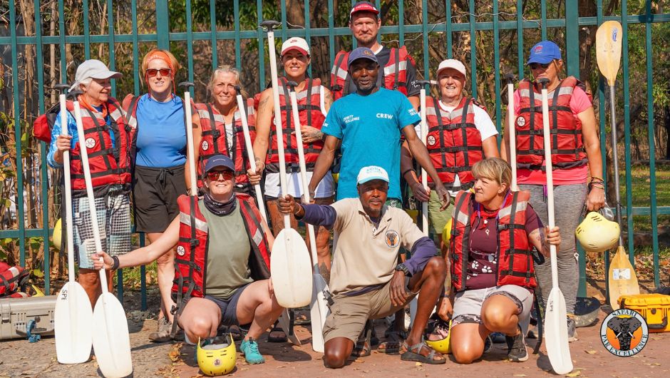 A group of people posing for a photo, wearing life jackets and holding paddles.