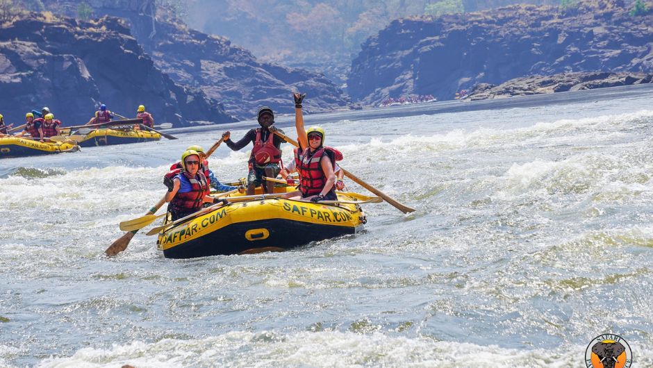 A group of people rafting down the zambezi river in a yellow raft.