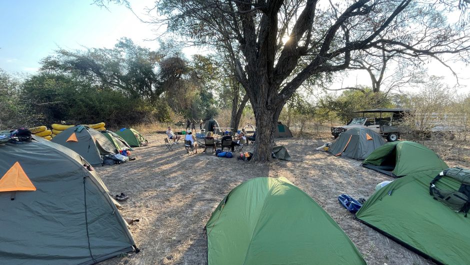 A group of tents arranged in a circle surrounding a group of people sat on camping chairs in a circle.