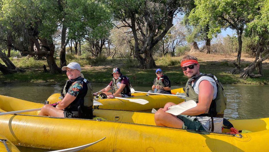 A group of people sat smiling in inflatable yellow kayaks, on the zambezi river.