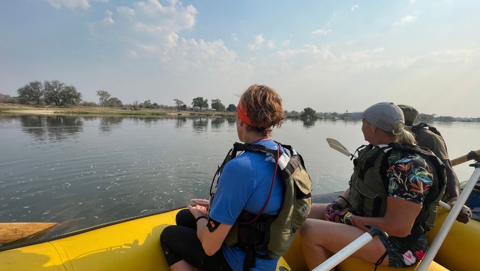 Three people looking at elephants on the bank of the zambezi river from their kayak.