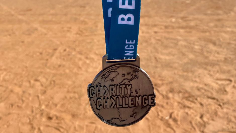 a charity challenge medal held up against a sandy backdrop