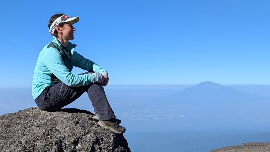 a person sitting on a rock in Tanzania, with Kilimanjaro in the background