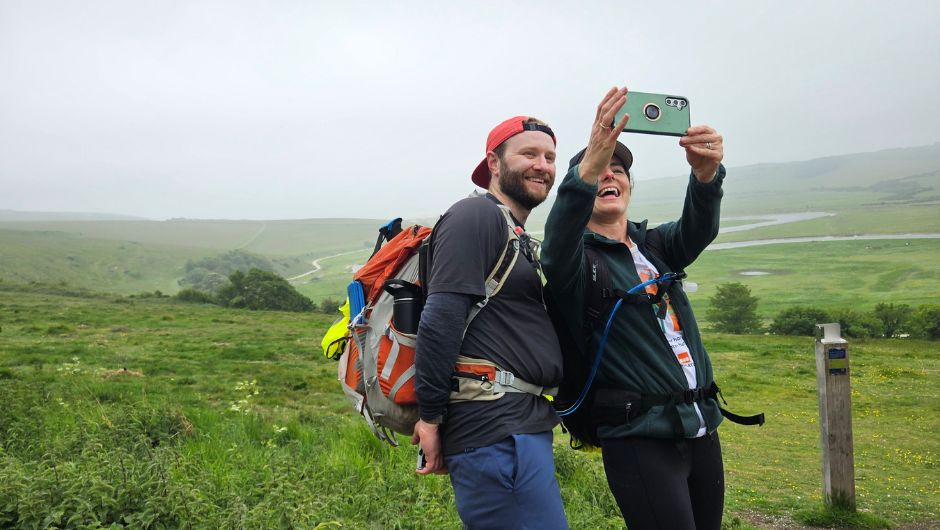 two trekkers during a challenge stopping to take a selfie against a green and misty background