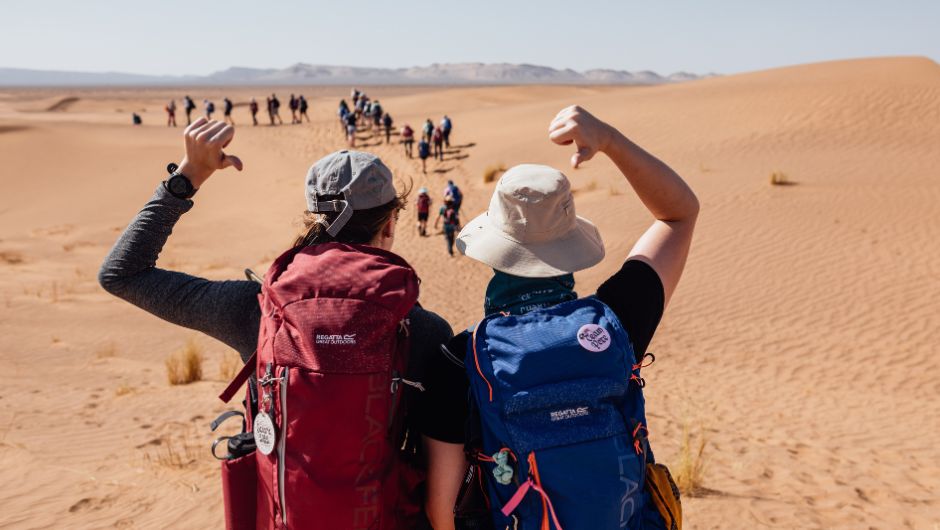 two trekkers on the sahara desert trek pointing to their backpacks