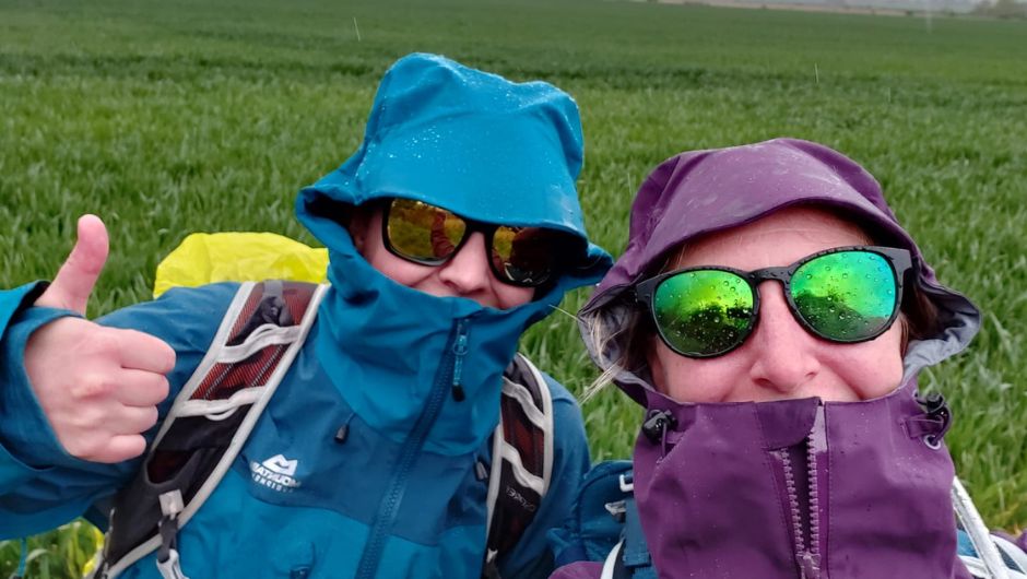 two people trekking in the rain, wearing waterproof jackets and sunglasses